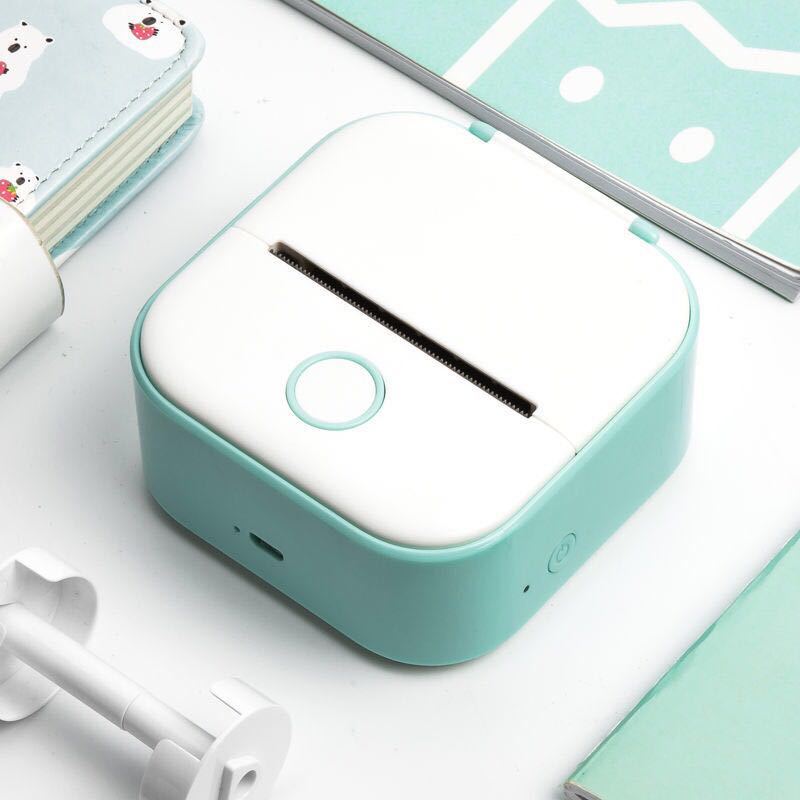 Teal and white electronic device on a light blue surface with stationery items.